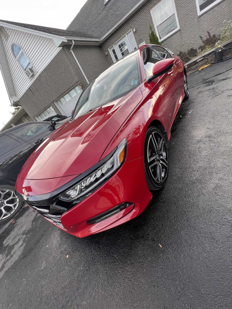 Red sedan with glossy exterior and clean wheels after a detailing package, parked on a residential driveway.| none | mobile hand wash | rinse and dry | gloss enhancement