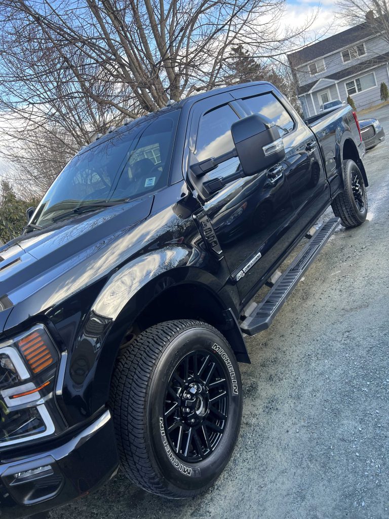 Black pickup truck with polished paint and clean wheels after a detailing package, parked curbside.| none | mobile hand wash | rinse and dry | wheel and tire shine